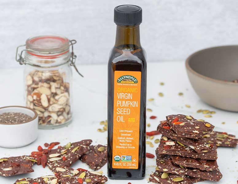 Chocolate Pumpkin Seed Superfood Bark stacked next to a bottle of pumpkin seed oil