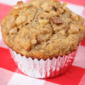 A Gluten Free Banana Walnut Muffin in a tin wrapper is placed on a white and red checkered placemat.
