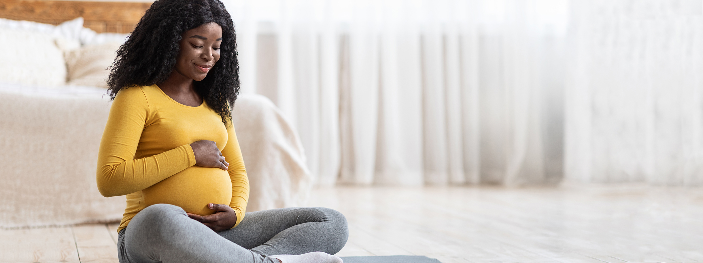 Dark Skinned Pregnant woman sitting on yoga mat. 