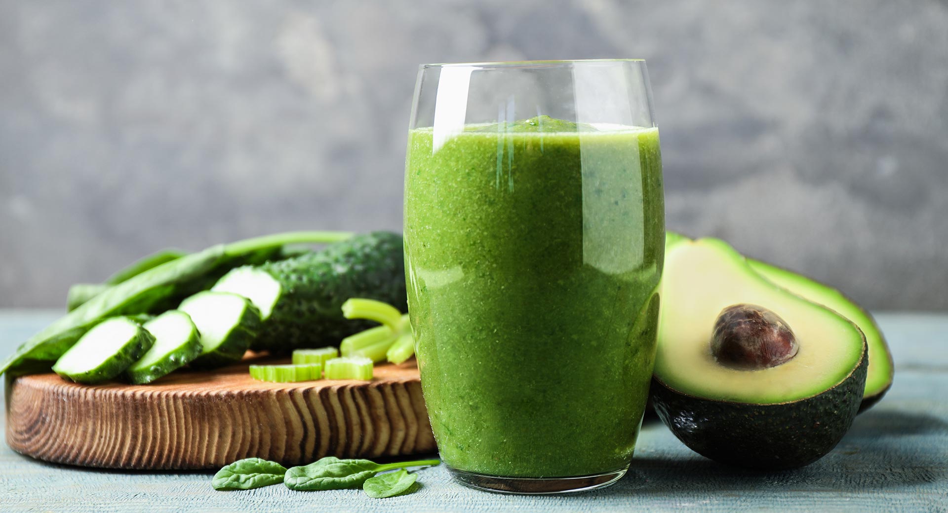 green smoothie in glass, cut avocado and cucumbers next to it