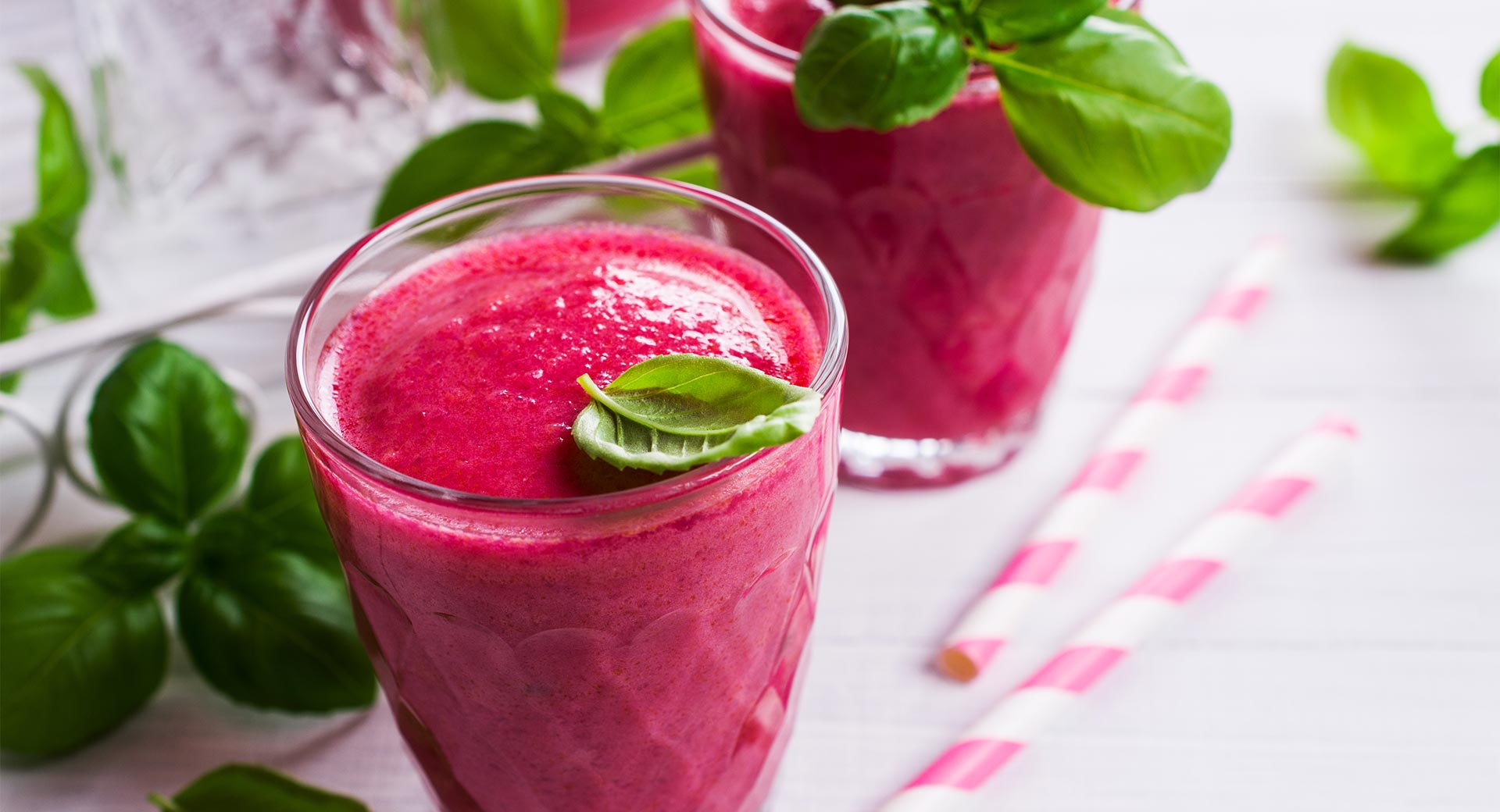red beet and berry smoothie in a glass with spinach garnish