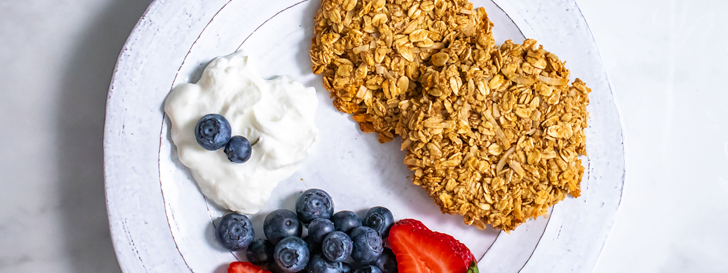 overhead view of white plate with coconut oat cookies, yogurt, blueberries and strawberries