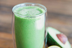 a mint green smoothie next to a halved avocado