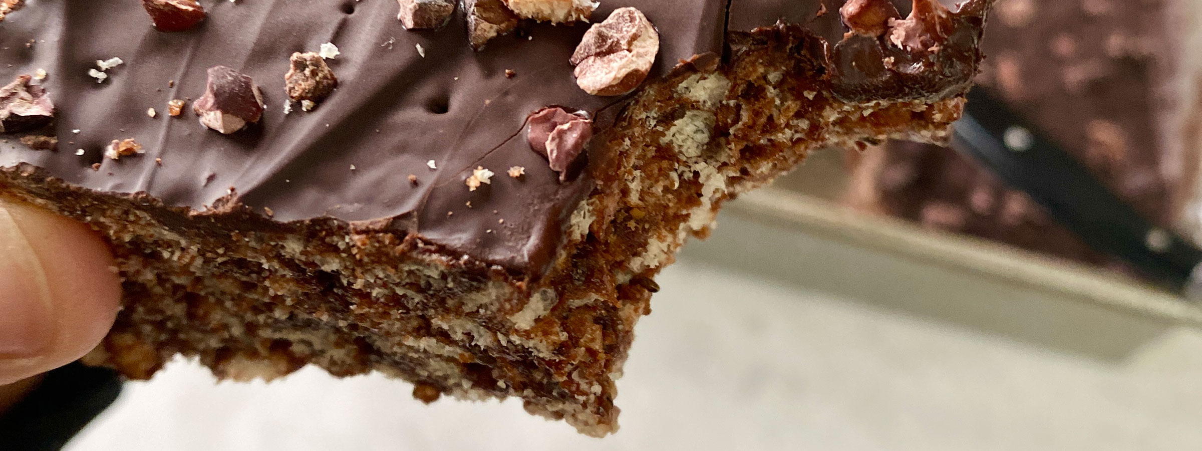 close up of a dark brown rice crispy treat being held above a tray of the same treats