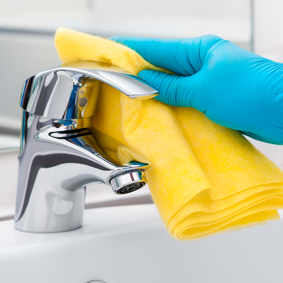 yellow towel cleaning a bathroom faucet wearing blue rubber gloves. 