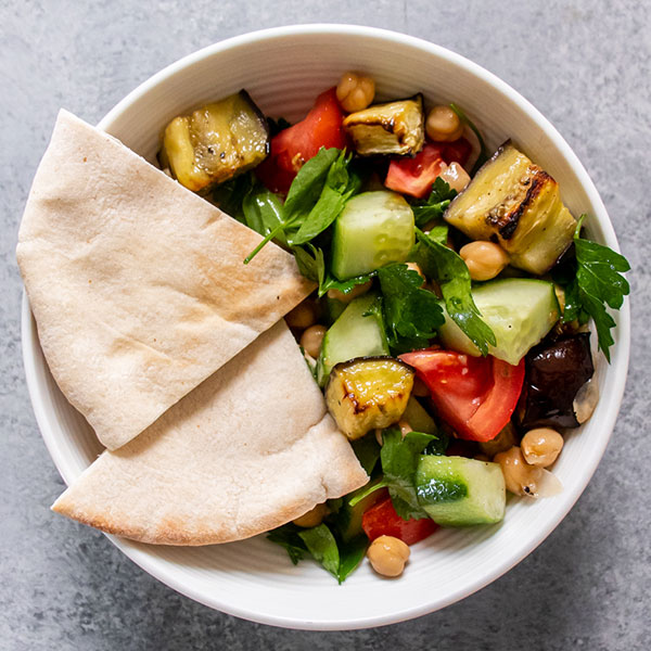colorful bowl of Mediterranean Eggplant Salad with two quartered slices of pita bread from overhead view