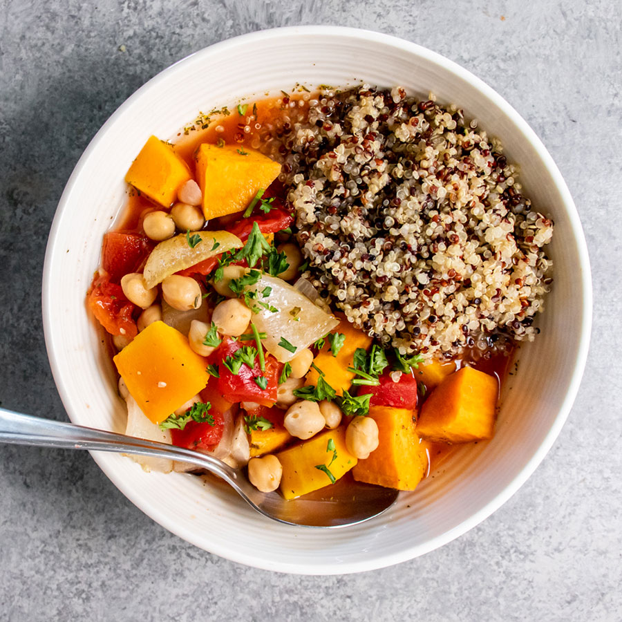 white bowl and spoon with colorful vegetable stew on one side and cooked quinoa on the other