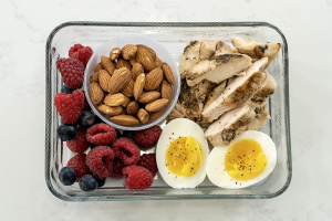 glass lunch container with grilled chicken, hard boiled egg, almonds and mixed berries