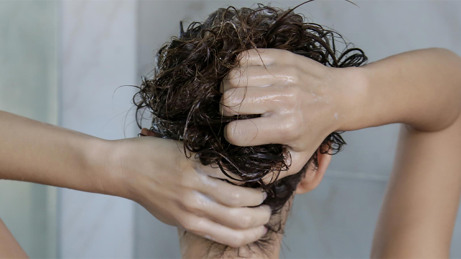 light skinned female presenting person with their back to camera washing their dark brown hair