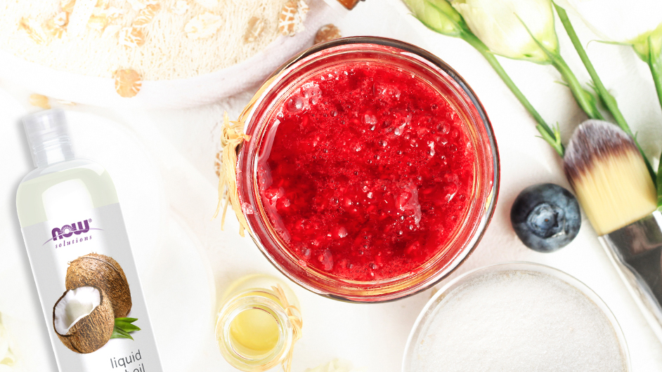 top view of red sugar scrub next to various beauty tools including NOW coconut oil