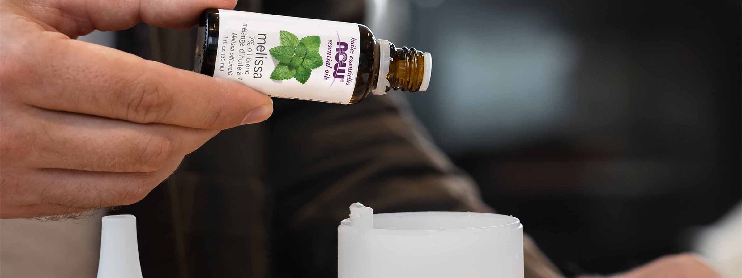 light skin male presenting hand pouring NOW Melissa Essential Oil into diffuser