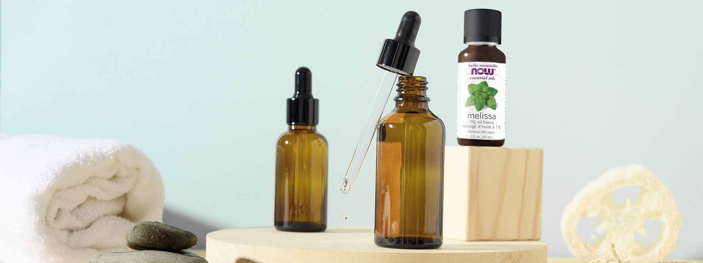 blue backdrop with two oil droppers and a bottle of NOW Melissa Oil