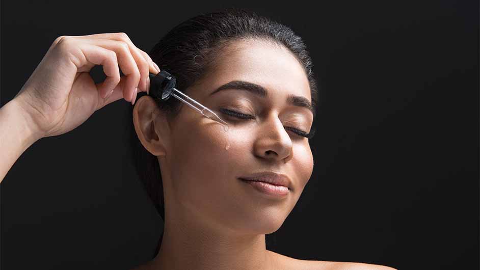 light-skinned, female-presenting person applying drops of skin serum to her face