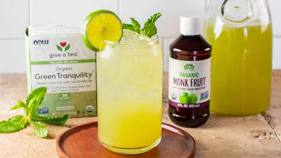 stone countertop with a glass of Citrus Cucumber and Mint Refresher and a box of NOW Green tea and NOW Monk Fruit Liquid