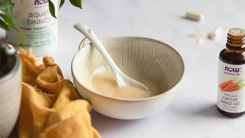 bowl of Cooling Collagen Face Mask next to NOW® Carrot Seed Essential Oil and a bottle of NOW® Solutions Aquatic Beauty+™ in the background