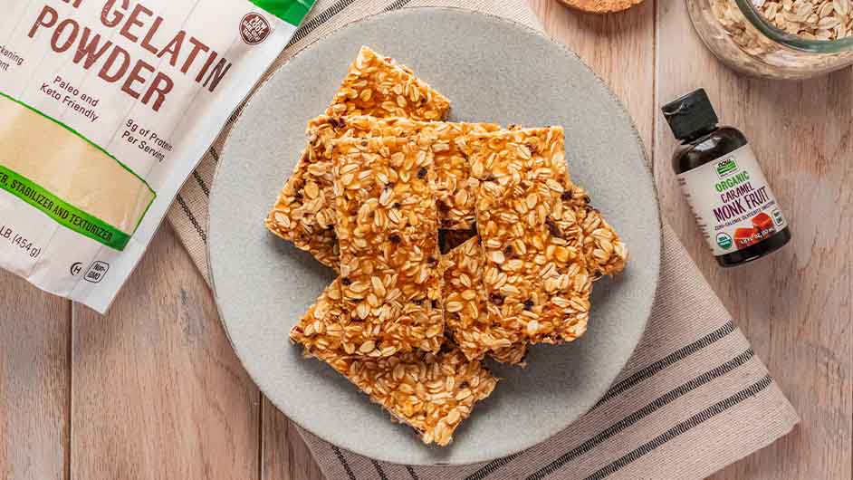 top view of plate with No-Bake Caramel Protein Bars between a bag of NOW Beef Gelatine and NOW liquid monk fruit caramel