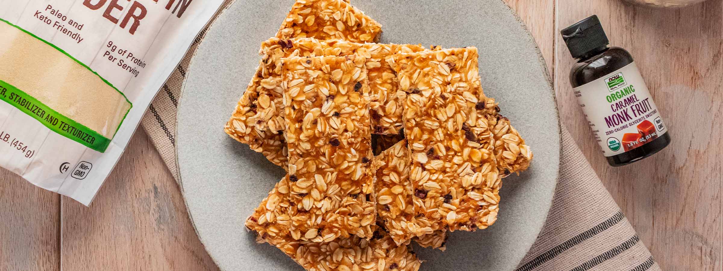 top view of plate with No-Bake Caramel Protein Bars between a bag of NOW Beef Gelatine and NOW liquid monk fruit caramel