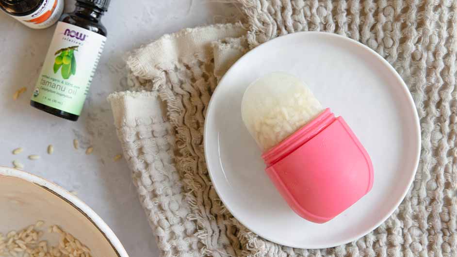top view of Rice Water Recovery Ice Roller next to a bottle of NOW® Solutions Organic Tamanu Oil, all on a brown terry cloth