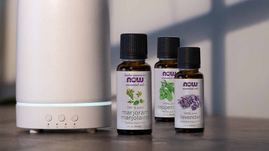 white essential oil diffuser next to three bottles of NOW Essential Oils