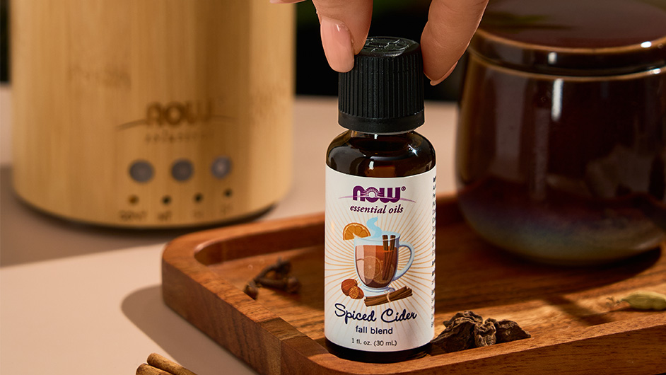 close up shot of NOW Spiced Cider Essential Oil with fingers grabbing the top