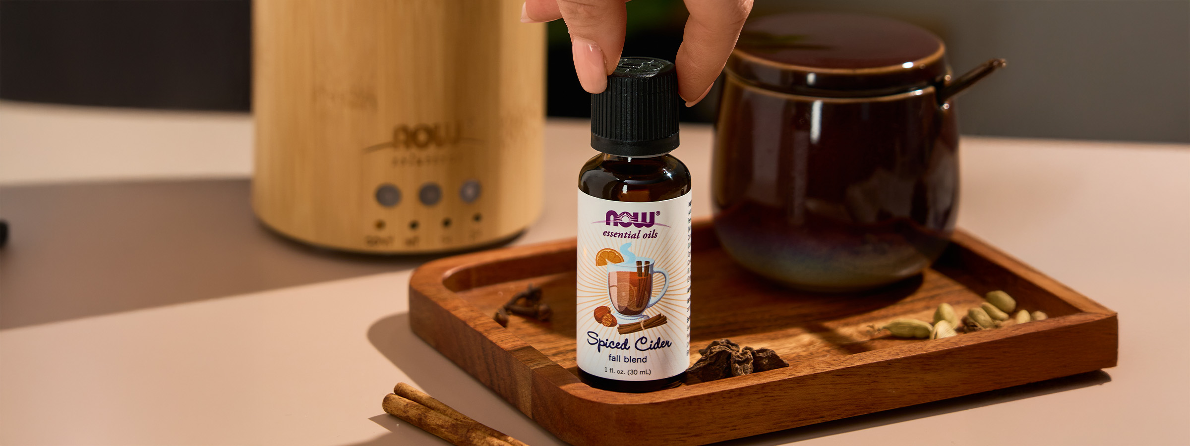 close up shot of NOW Spiced Cider Essential Oil with fingers grabbing the top