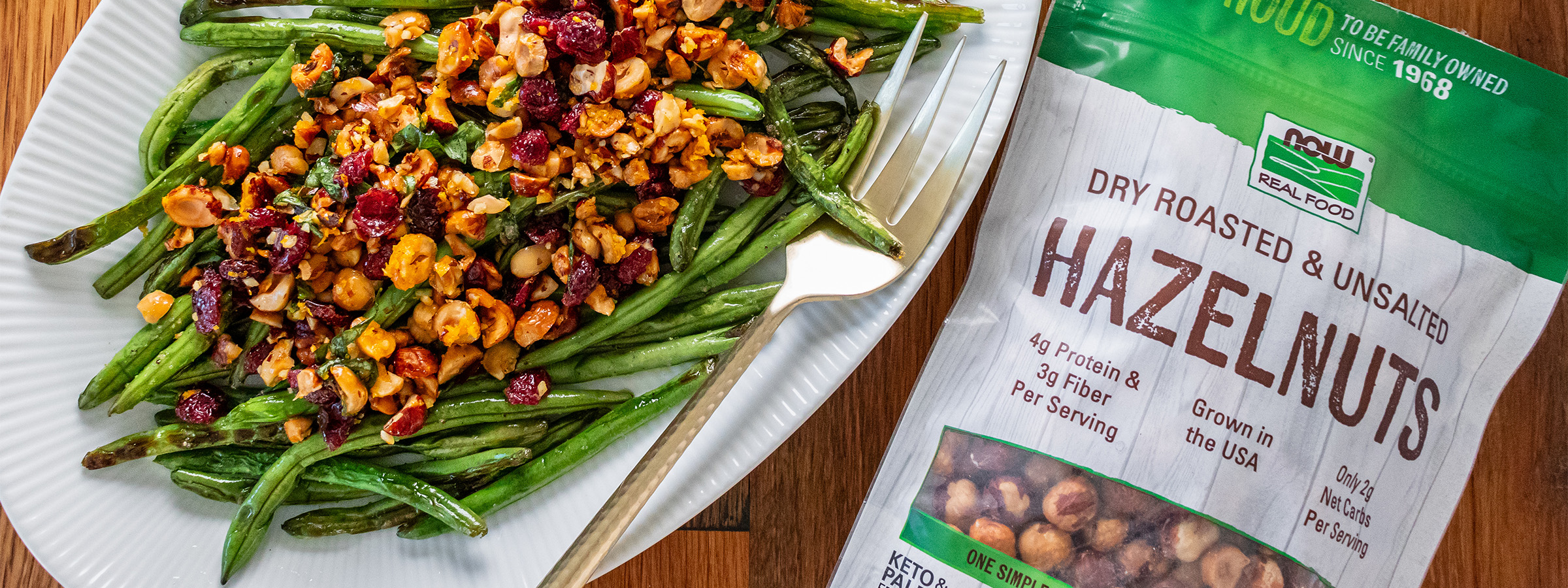 top view of Charred Green Beans with Hazelnut Topping next to a bag of NOW hazelnuts