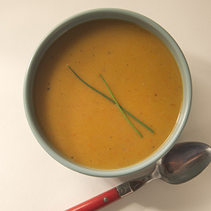 A light green ceramic bowl on a white table with Butternut Squash Soup in it and a spoon nearby.