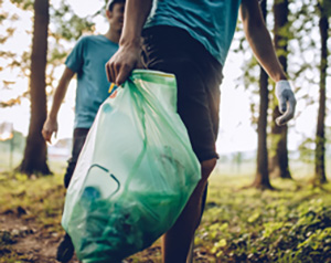 Person picking up trash in a forest preserve, holding a garbage bag