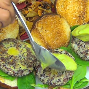 A hand offscreen scoops lime-green Avocado Puree onto a plate of Quinoa and Chia Sliders.