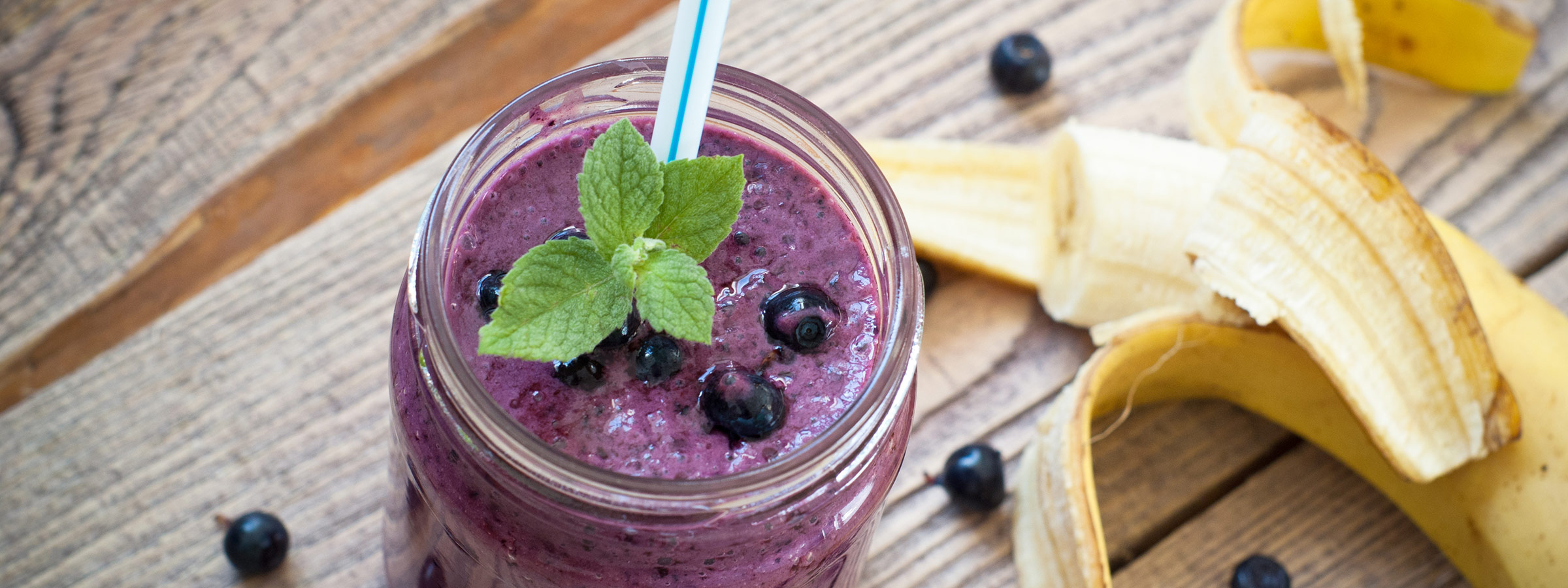 A mason jar on a wooden table is filled with a purple Berry Blast Smoothie