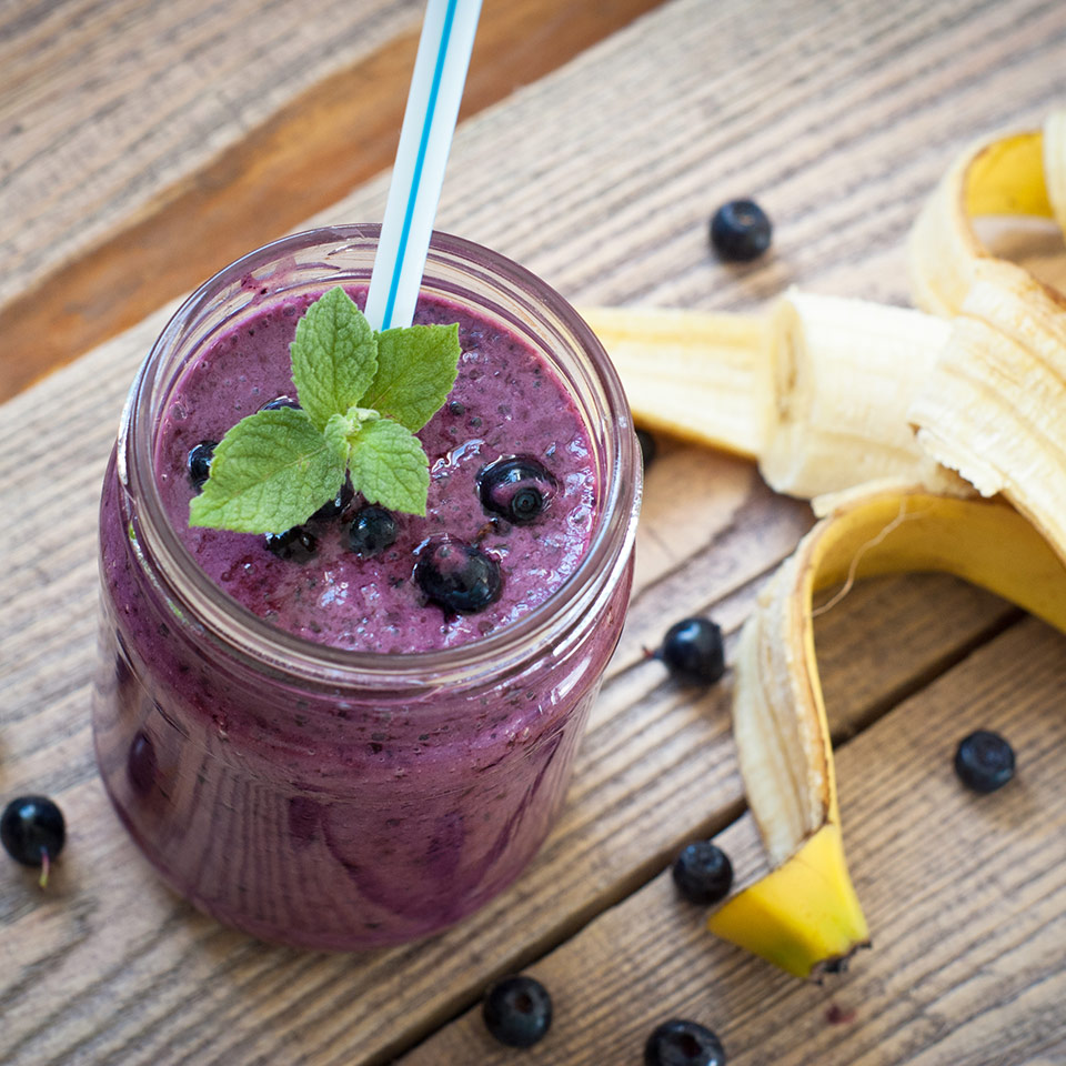 A mason jar on a wooden table is filled with a purple Berry Blast Smoothie