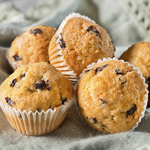 Several fluffy Blueberry Flax Muffins are placed on a table in their wrappers.