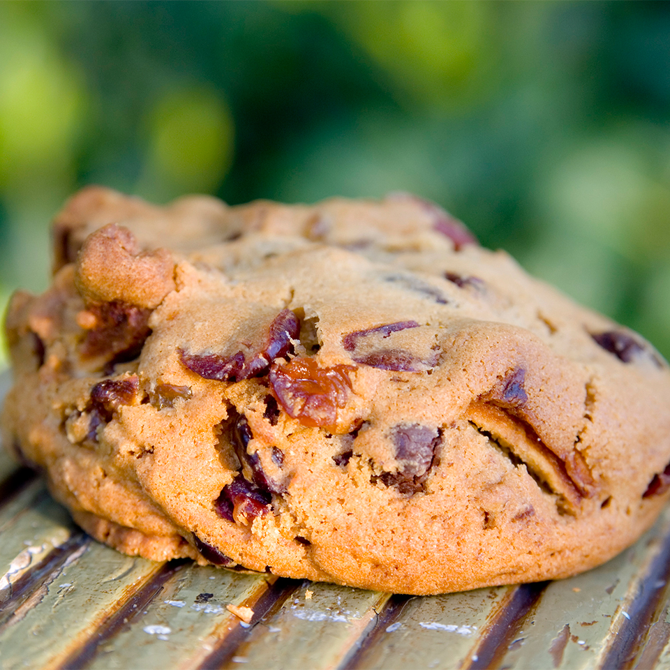 A Chocolate Cherry Blondie Cookie sits on a wooden table outdoors.