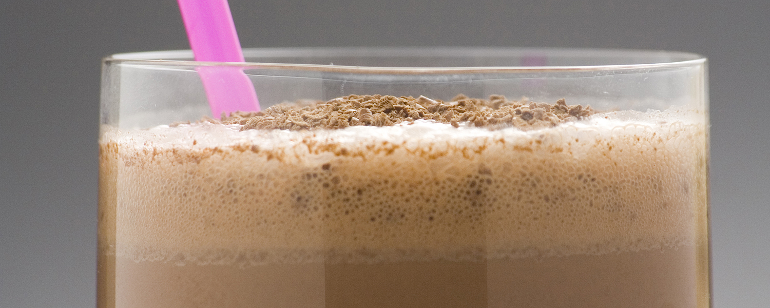 A drinking glass with a bright pink straw is filled with a brown Cinnamon Chocolate Protein Shake.