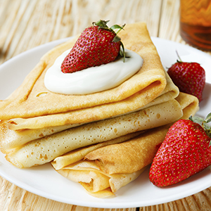 A white ceramic plate on the wooden table is holding Coconut Flour Crepes