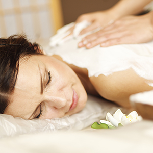 A female-presenting person lying face down, relaxed, receiving a massage with Cooling Body Scrub.