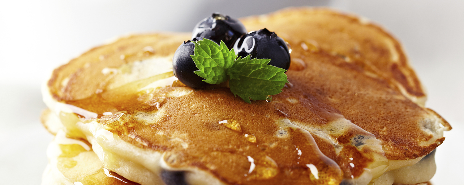 A stack of Gluten Free Cinnamon Blueberry Pancakes topped with blueberries and syrup.