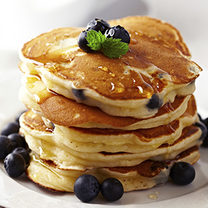 A stack of Gluten Free Cinnamon Blueberry Pancakes topped with blueberries and syrup.