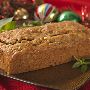 A loaf of Gluten-Free Holiday Fruitcake is placed on a dark brown plate