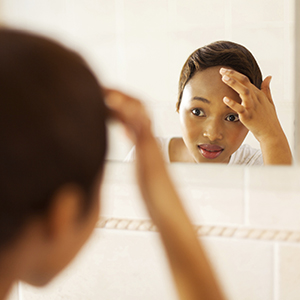 A female-presenting person with dark skin and short brown hair looking at themselves in the mirror