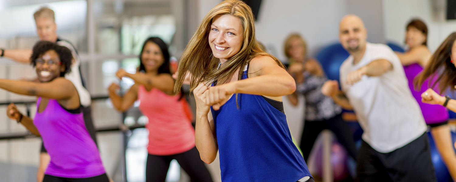 A female-presenting person with light skin, blonde hair and an athletic top leads a kickboxing class