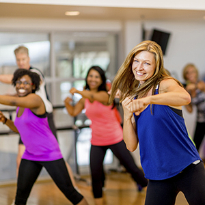 A female-presenting person with light skin, blonde hair and an athletic top leads a kickboxing class