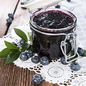 A mason jar on a wooden table is holding several servings of Sugar Free Blueberry Preserves