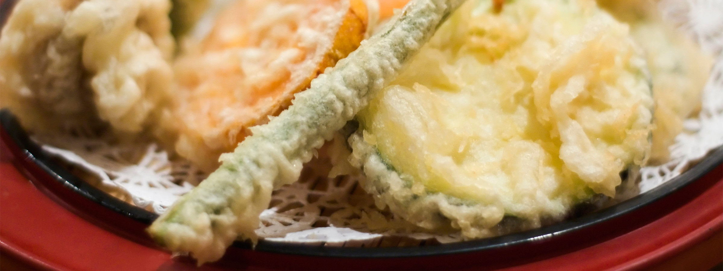 A closeup of a serving of Gluten Free Vegetable Tempura on a black and red plate.