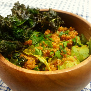 A wooden bowl on a white and blue placemat holds a serving of Thai Red Curry Quinoa Salad.