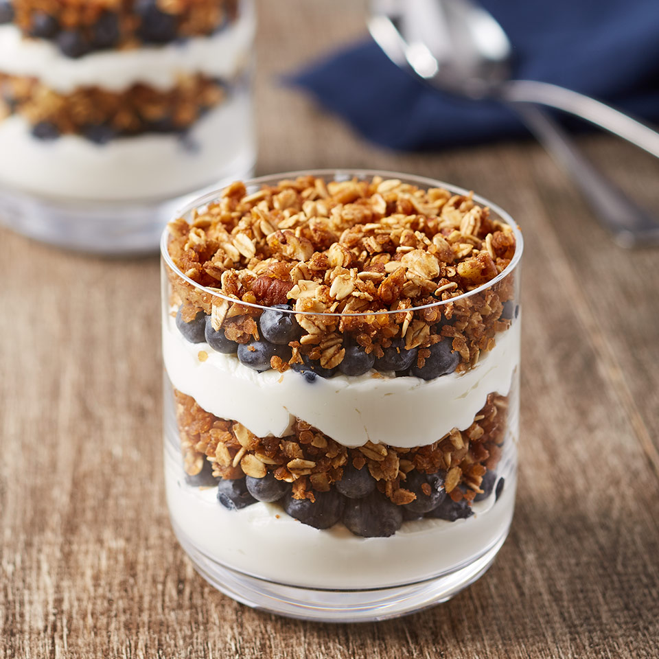 Two short glasses on a wooden table hold Toasted Manuka Honey Cinnamon Granola Parfaits