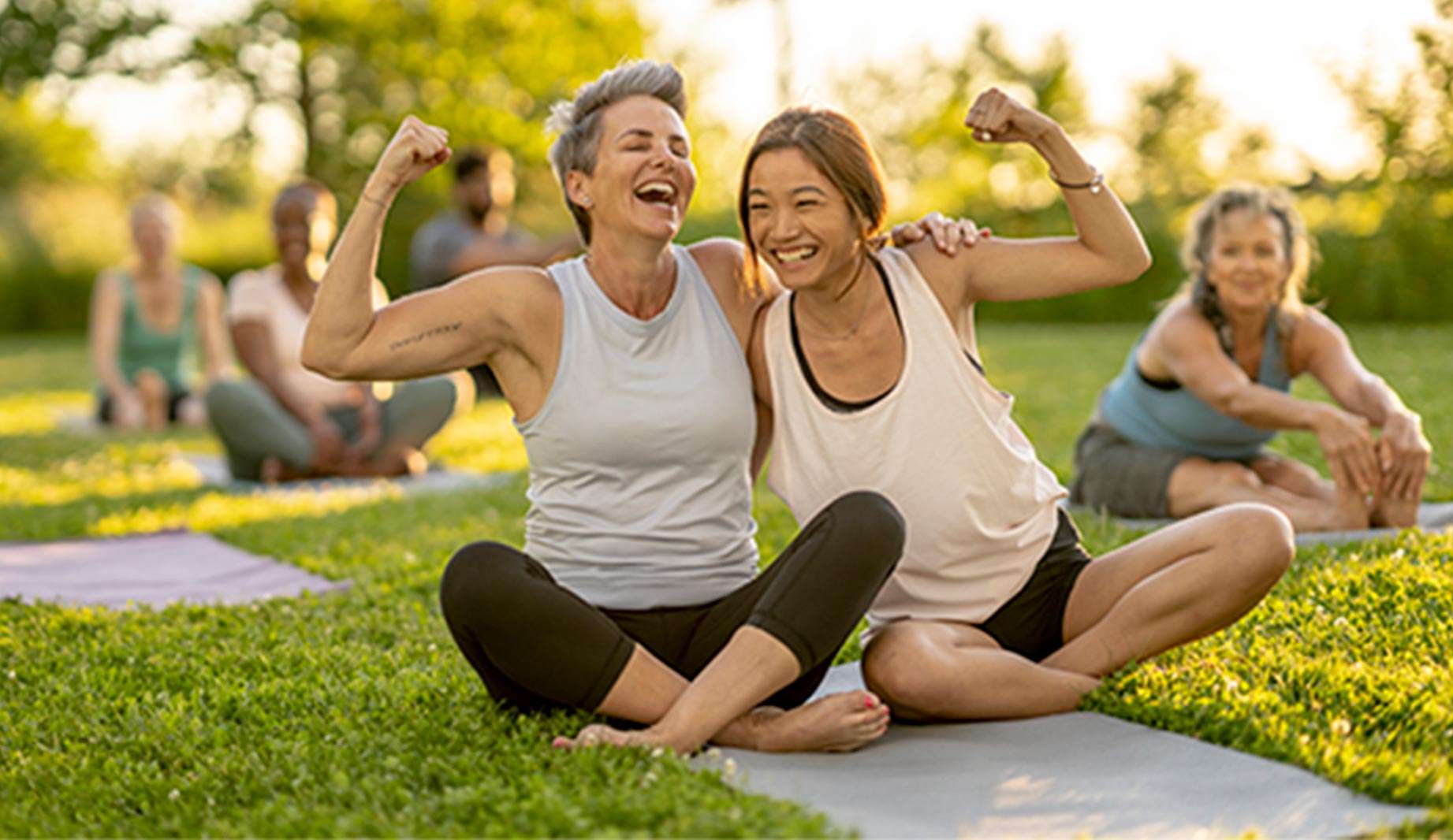 female presenting persons sitting on a yoga mat smiling and flexing their arms