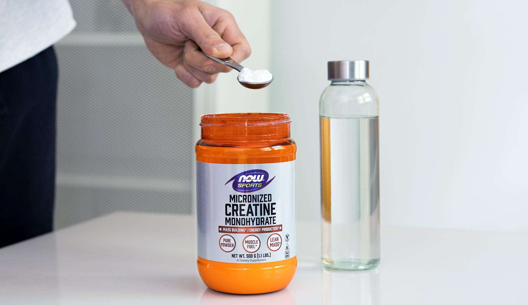 NOW Sports Micronized Creatine Monohydrate, bottle of water, hand holding scoop of powder.
