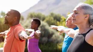 four people in workout clothes various races and sex standing outdoors with arms stretched and eyes closed