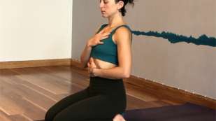 presenting as woman with black yoga pants and green sports top kneeling on a mat in a room with wood floors and white walls